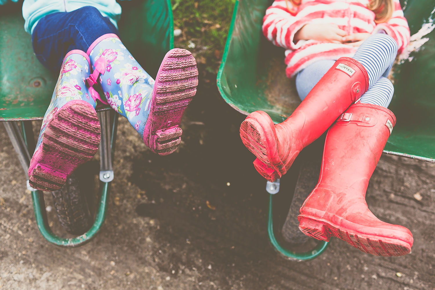 Children sitting in a wheel barrow with wellies on