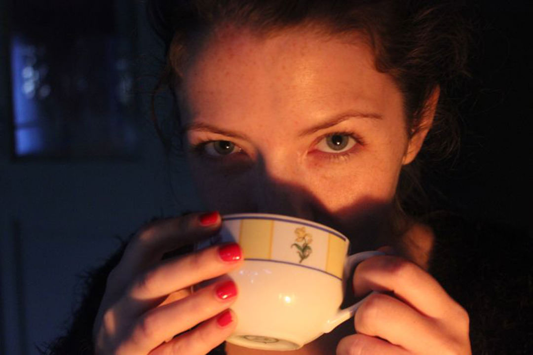 A lady with a cup of tea lit by candlelight